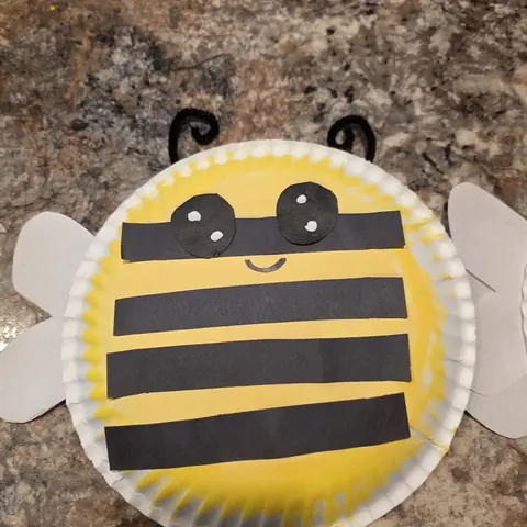 A paper-plate bumblebee craft with black stripes, googly eyes and paper wings