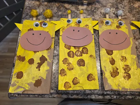 Three paper giraffe crafts with googly eyes and brown fingerprint spots