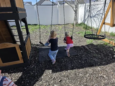 Two small children on the backyard swings, seen from behind