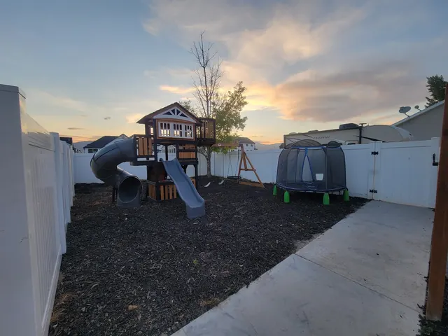 The Hangar's fenced backyard at sunset: a wooden playset with a slide, swings, a small trampoline and a playhouse